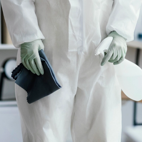 Technicien en combinaison de protection tenant un produit de traitement et un chiffon, prêt à intervenir pour une désinsectisation contre les punaises de lit.