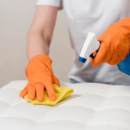 Nettoyage et traitement d’un matelas contre les punaises de lit, personne portant des gants pulvérisant un produit désinfectant et essuyant la surface.