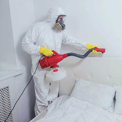 Technicien spécialisé en combinaison de protection réalisant un traitement thermique contre les punaises de lit dans une chambre, à l’aide d’un appareil professionnel.