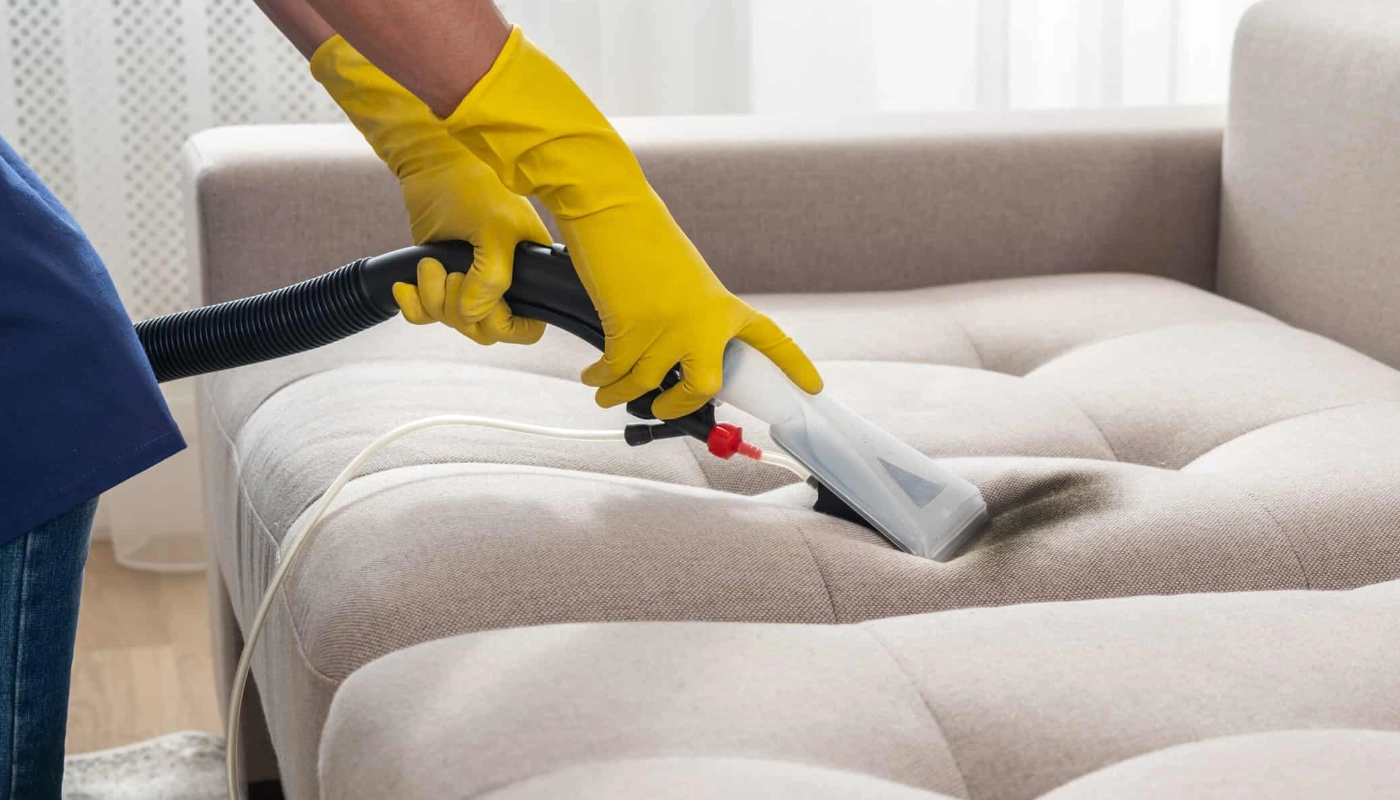 Nettoyage et traitement d’un canapé à l’aide d’un aspirateur injecteur-extracteur, porté avec des gants de protection pour éliminer les punaises de lit.