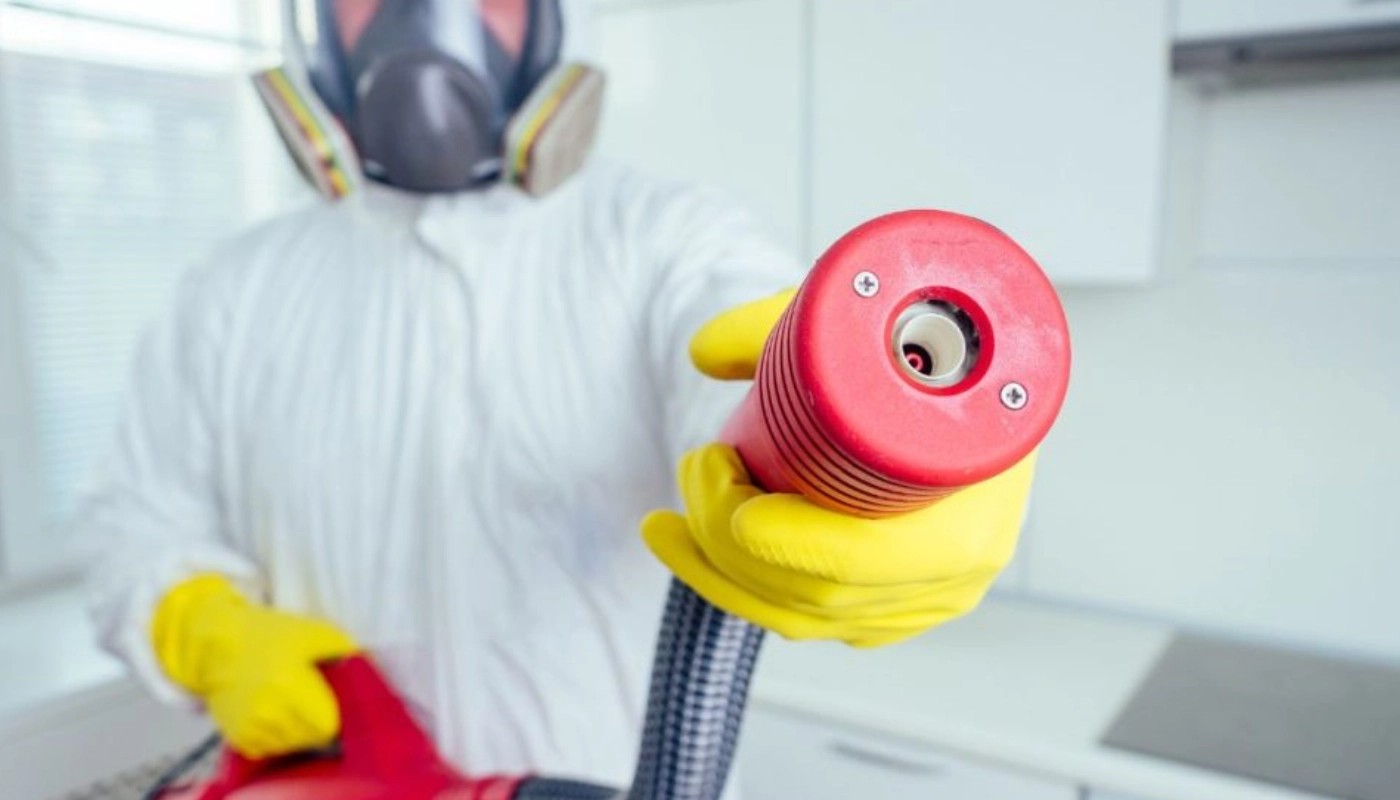 Le geste simple à adopter chaque soir pour éviter la punaise de lit 14 Technicien en combinaison de protection et masque respiratoire utilisant un appareil professionnel pour le traitement des punaises de lit, garantissant une intervention sécurisée et efficace.